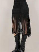 Black fringe skirt with sheer panels worn with black boots on a neutral background