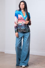 Woman wearing a colorful blazer and blue pants against a white background