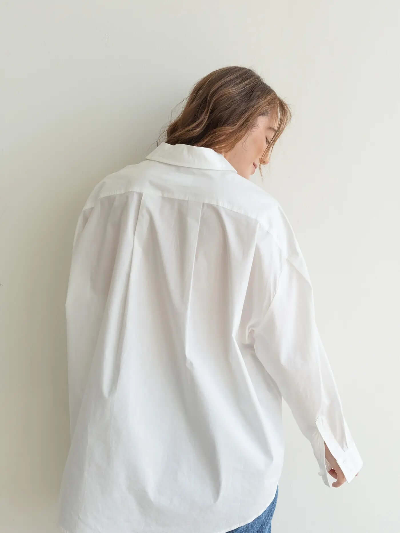 Woman in a white shirt and blue jeans standing in a bright room with a vase of flowers on a small table.