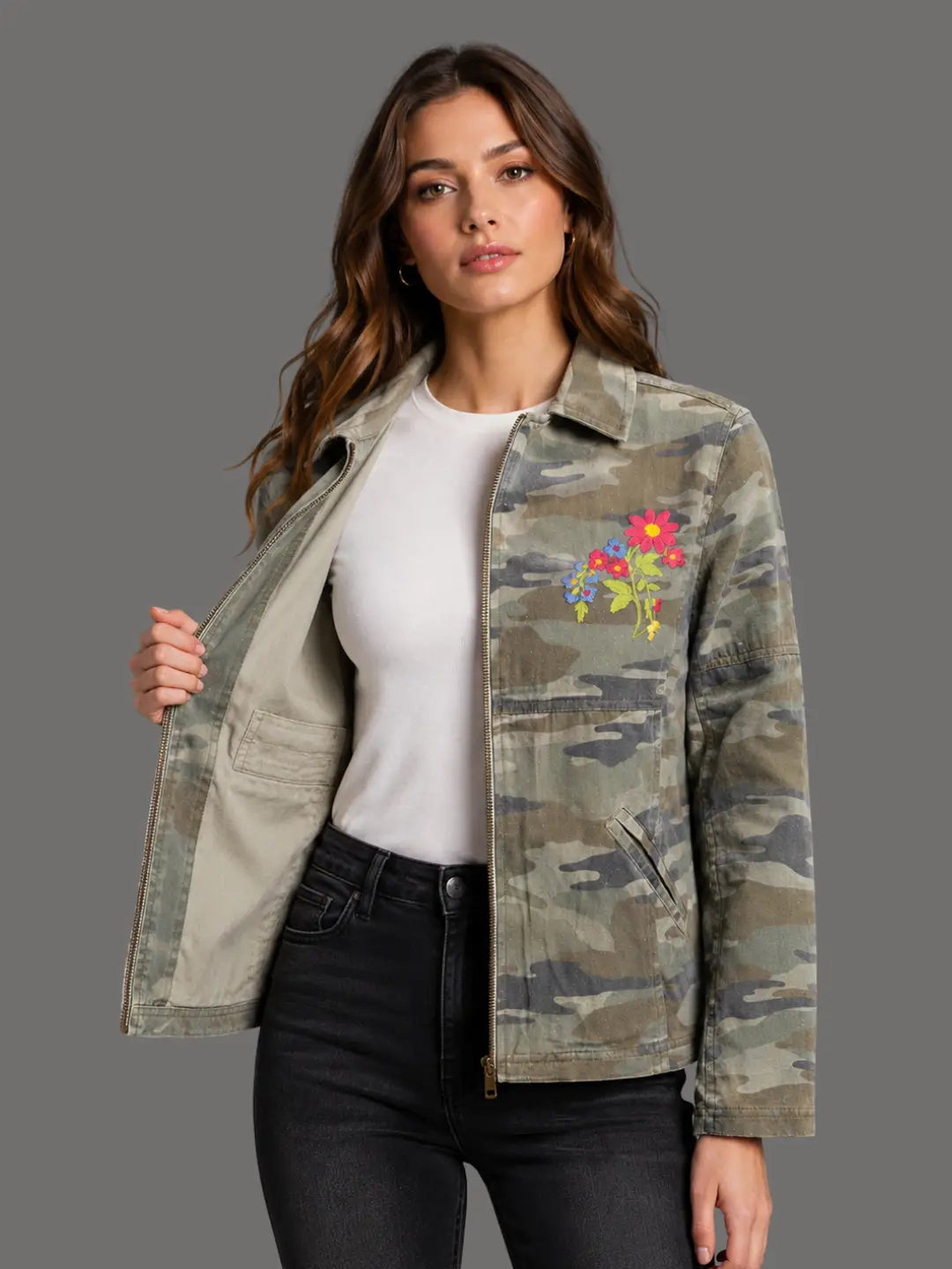 Woman wearing a camouflage jacket with floral embroidery on a gray background