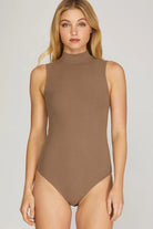 Woman wearing a brown high neck sleeveless bodysuit against a plain background