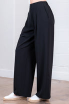 Black wide-leg pants worn by a person against a white brick wall.