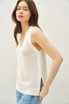 Woman wearing a white sleeveless knitted top against a plain background