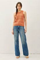 Woman wearing an rust sleeveless top and blue jeans on a white background