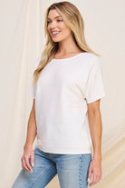 Woman wearing a white top and blue jeans against a beige background