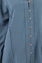 Close-up of dusty-blue striped shirt placket and chevron pinstripe detail with wooden buttons.