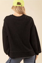Back of black textured knit oversized top showing drop shoulders and raw-edge hem on model.”