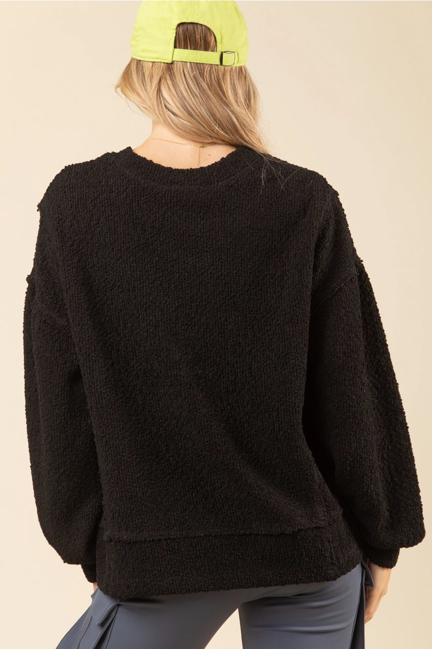 Back of black textured knit oversized top showing drop shoulders and raw-edge hem on model.”