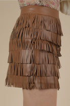 Side view of brown fringe mini skirt in vegan leather with multi-tier tassels