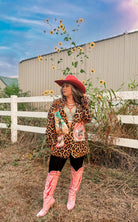 Person wearing a leopard print jacket and pink boots standing in a field with sunflowers and a barn in the background.