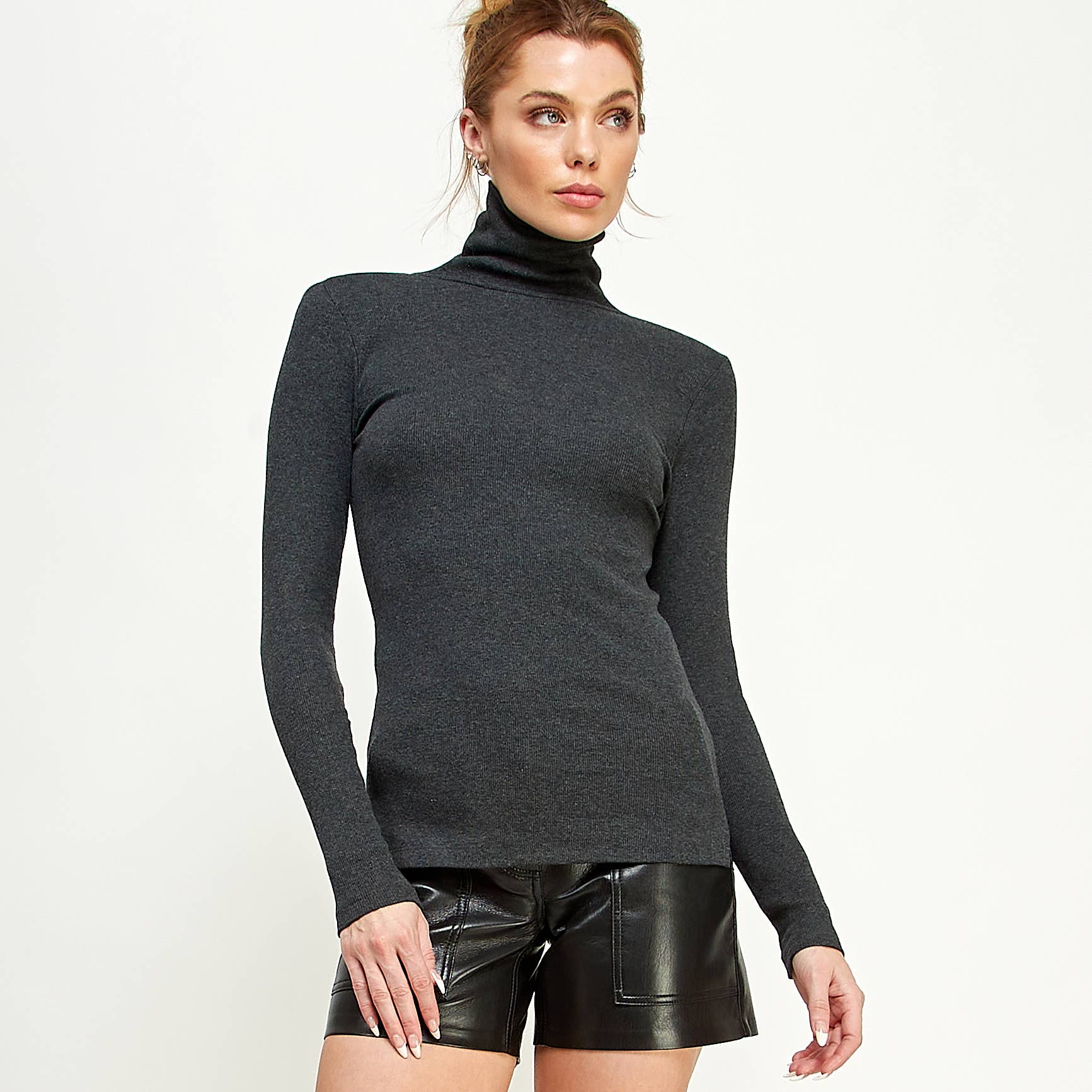 Woman wearing a dark gray turtleneck sweater and black leather shorts on a white background