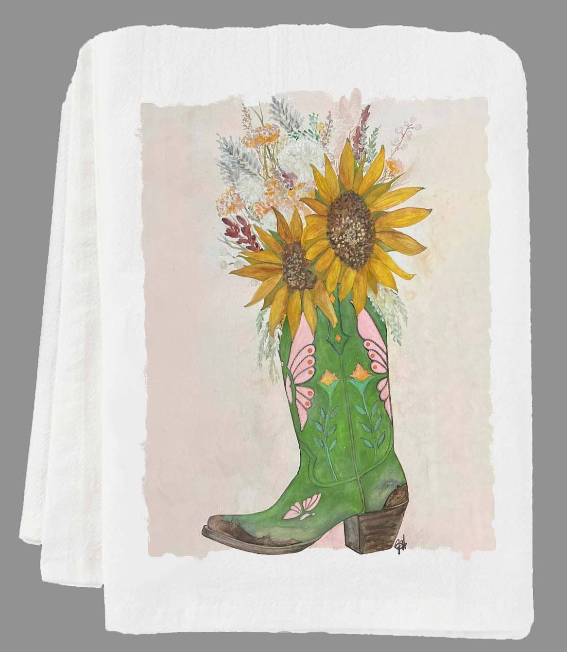 Green cowboy boot with sunflowers and floral design on a folded white tea towel.