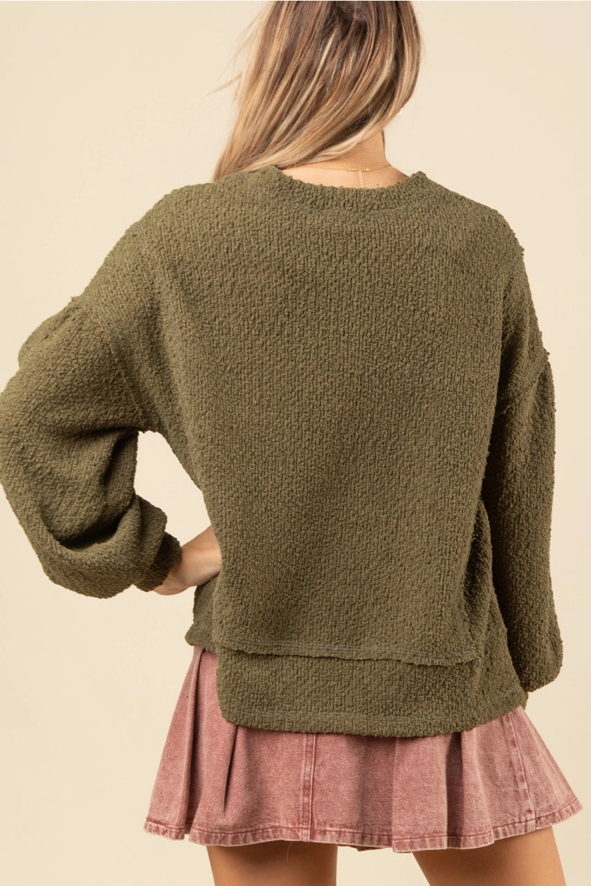 Back of olive textured knit oversized top showing drop shoulders and raw-edge hem on model.