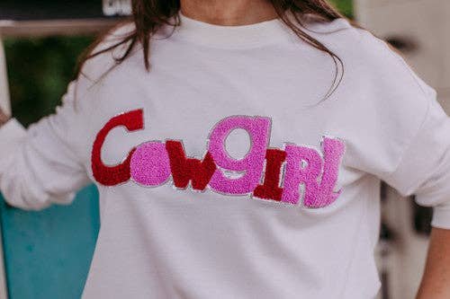 White sweatshirt with 'Cowgirl' text in red and pink on a blurred background