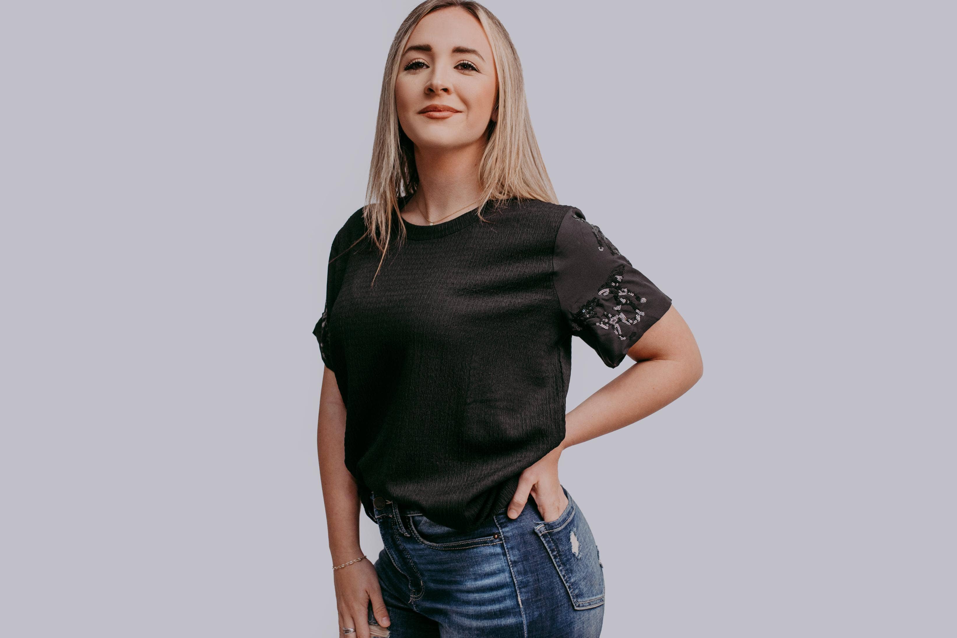 Woman wearing a black t-shirt with horse sequin details against a plain background