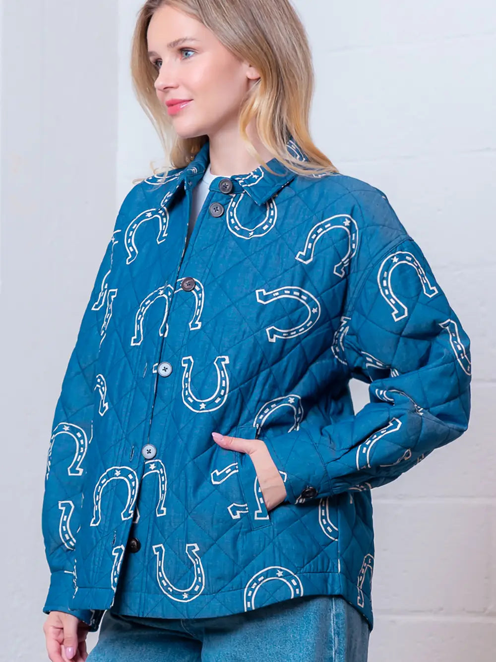 Front view of denim-blue quilted jacket with white horseshoe print and button front on model.