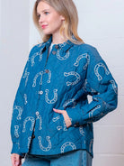 Front view of denim-blue quilted jacket with white horseshoe print and button front on model.