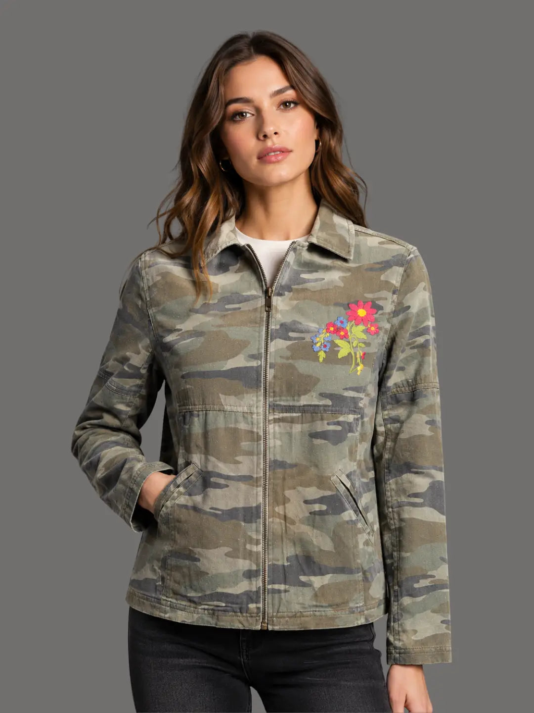Woman wearing a camouflage jacket with a colorful floral patch on a gray background