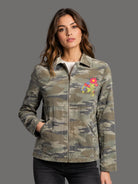 Woman wearing a camouflage jacket with a colorful floral patch on a gray background