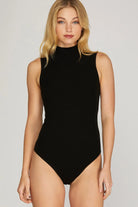 Woman wearing a black high neck sleeveless bodysuit on a plain background