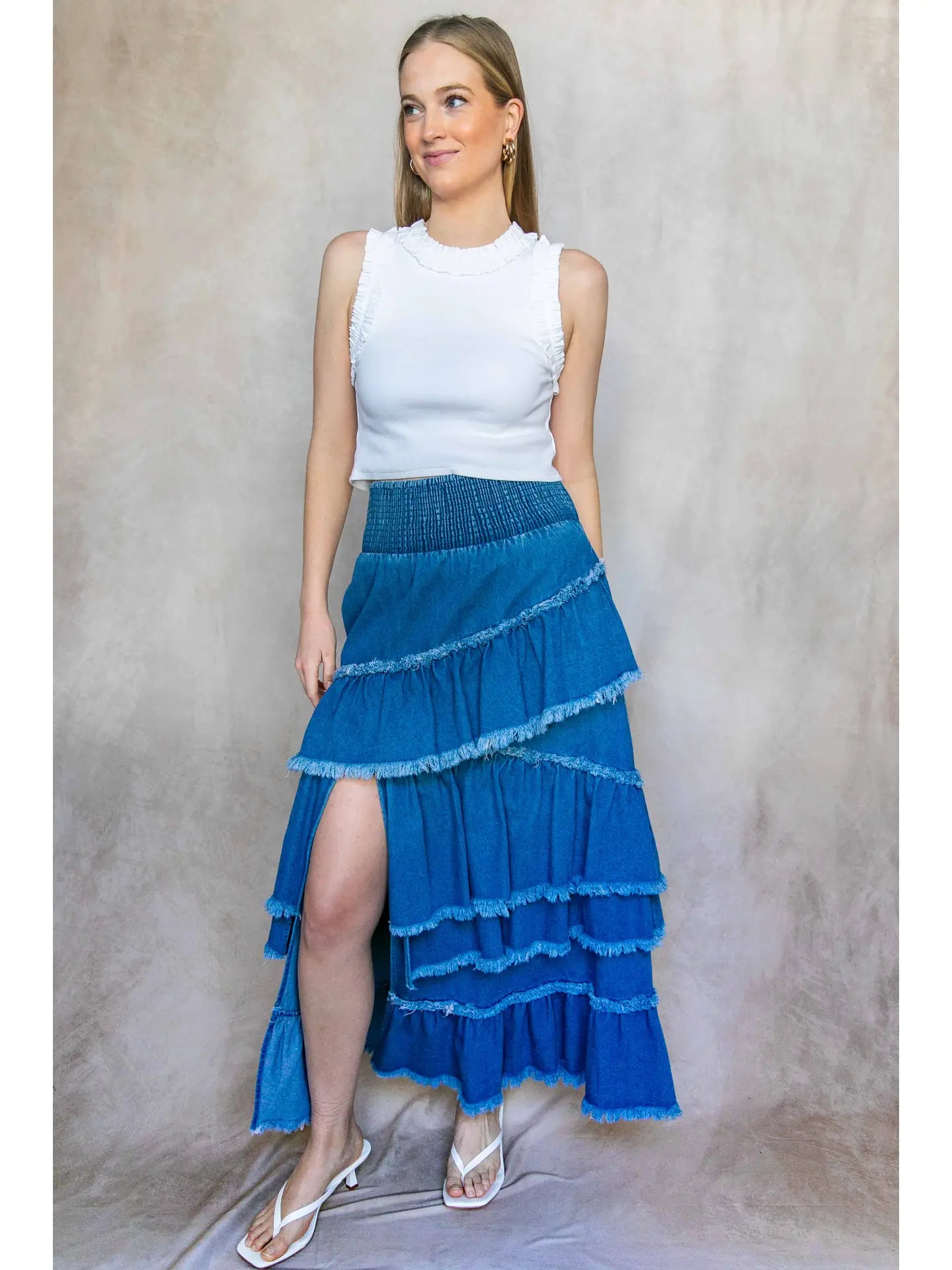 Woman wearing a white top and blue tiered skirt against a neutral background