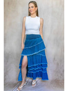 Woman wearing a white top and blue tiered skirt against a neutral background
