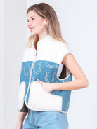 Model wearing indigo denim vest with white horseshoe print and faux-fur collar, zipped front, hands in pockets.”