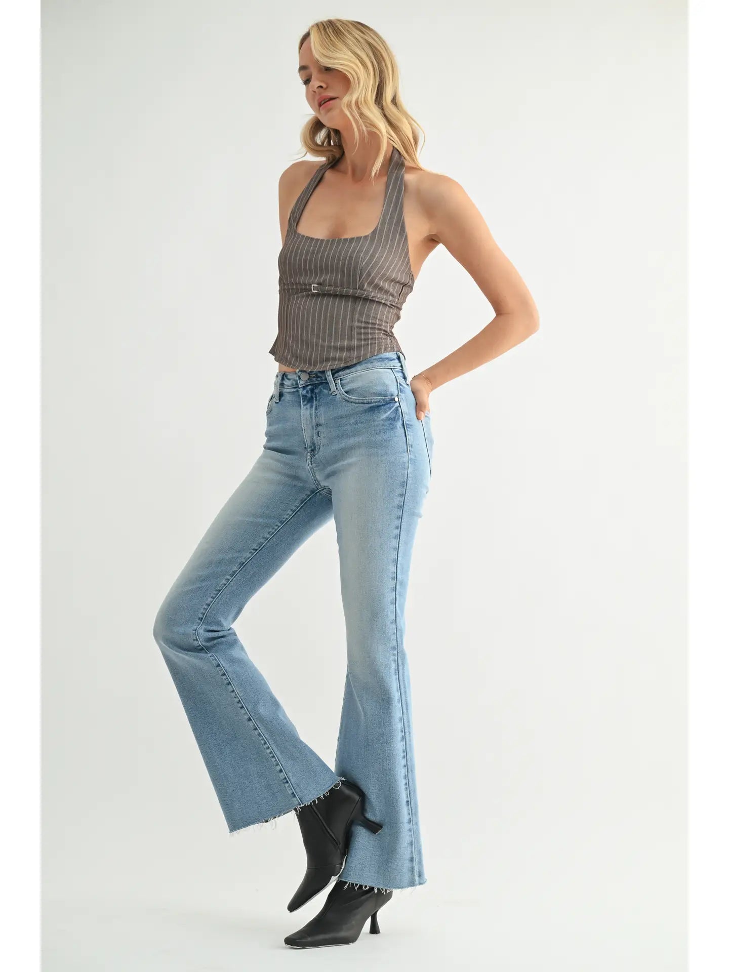Woman wearing a gray halter top and blue flared jeans on a white background