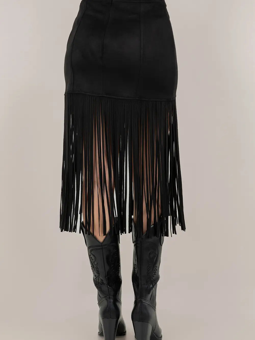 Black fringe skirt worn with black knee-high boots on a plain background