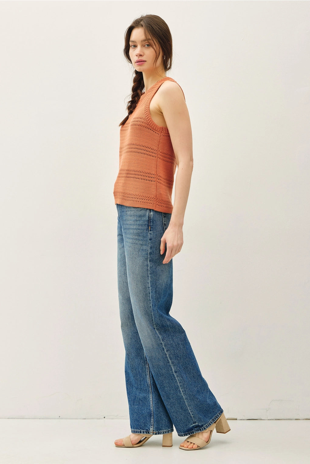Woman wearing an rust sleeveless top and blue jeans on a white background