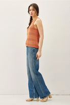 Woman wearing an rust sleeveless top and blue jeans on a white background