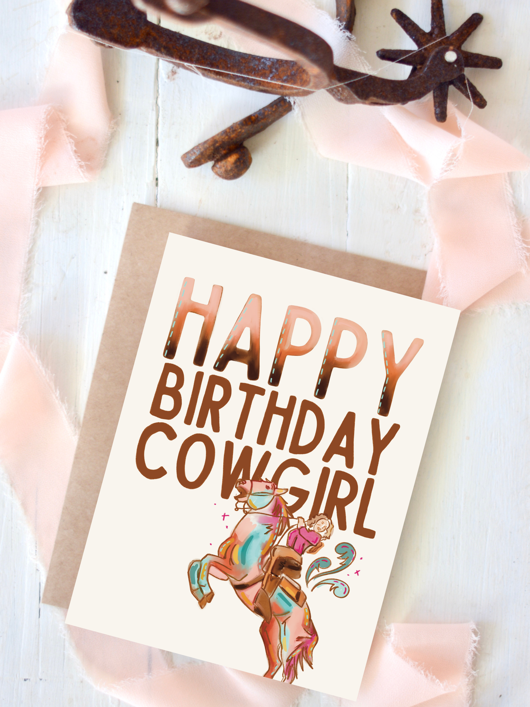 A greeting card with the text 'HAPPY BIRTHDAY COWGIRL' displayed in a bold, copper-colored font. The card features an illustration of a cowgirl riding a turquoise mustang.