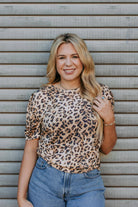 Woman wearing a leopard print top and blue jeans standing against a metallic background