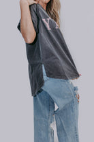 Person wearing a mineral gray short sleeve shirt with lettering and ripped jeans on a plain background