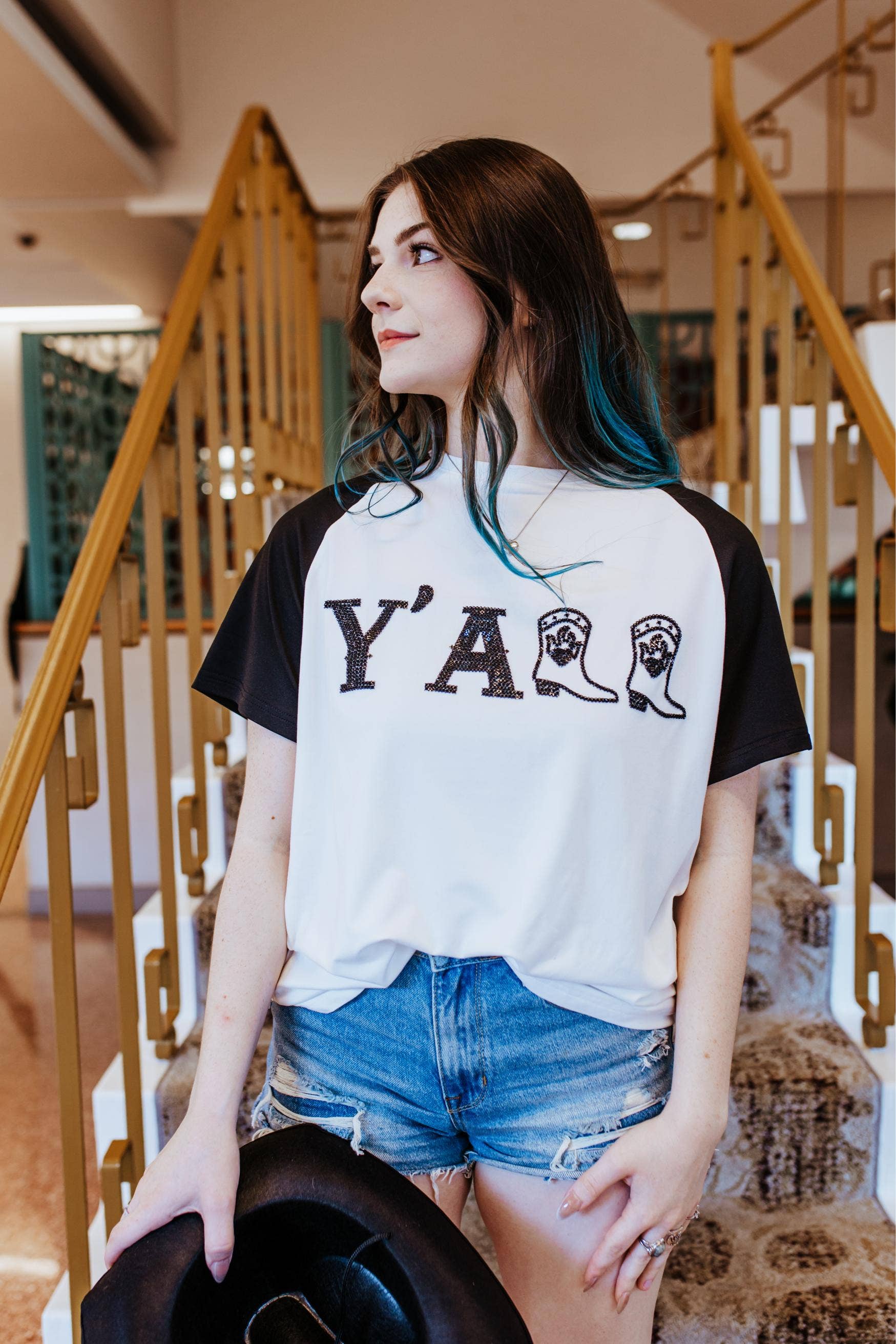 Woman wearing a white t-shirt with 'Y' ALL and boot graphic, standing in a staircase.