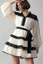 Woman wearing a white dress with black  ruffle accents on a plain background