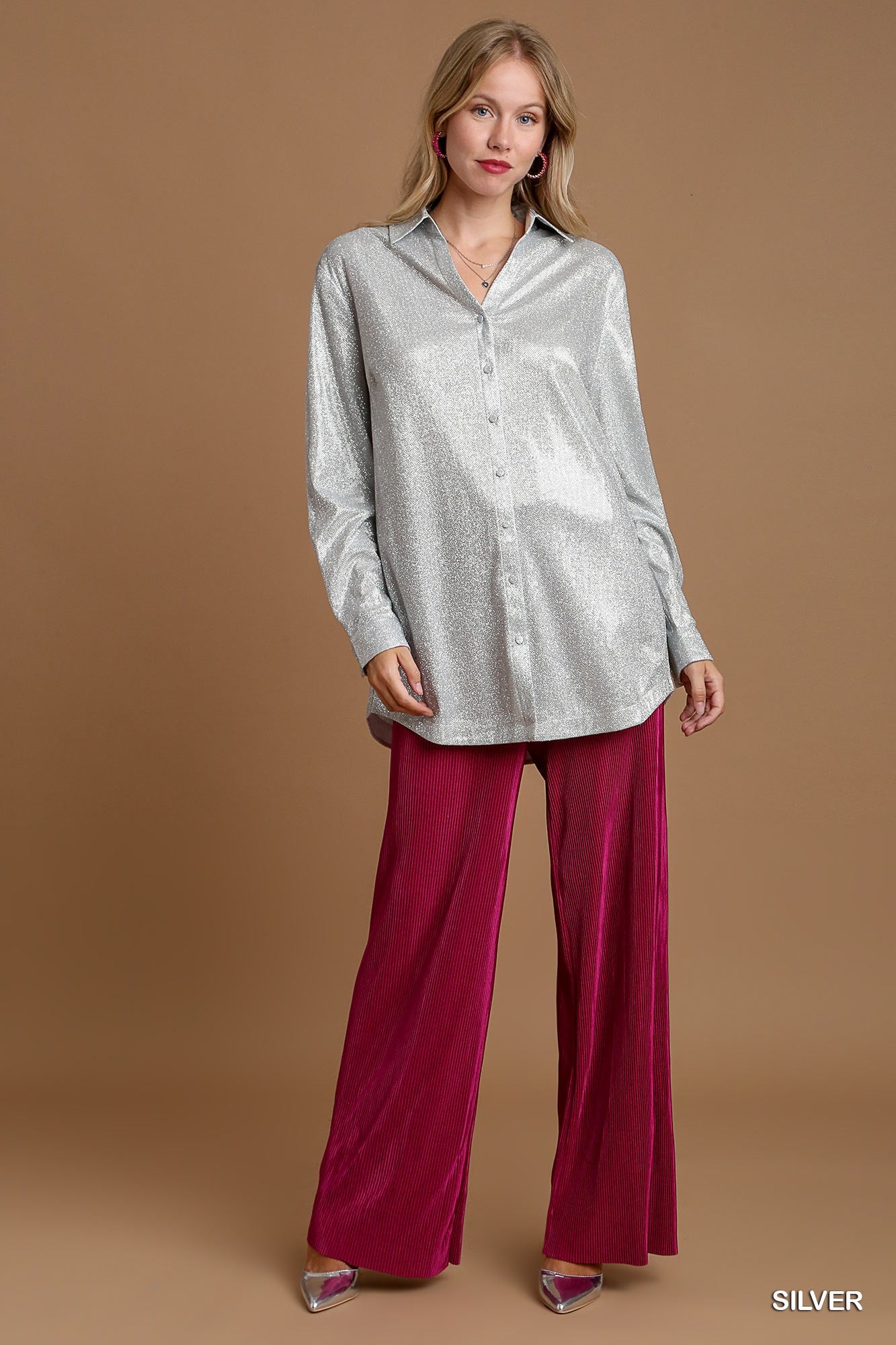 Woman wearing a silver button-up shirt and magenta pants on a brown background