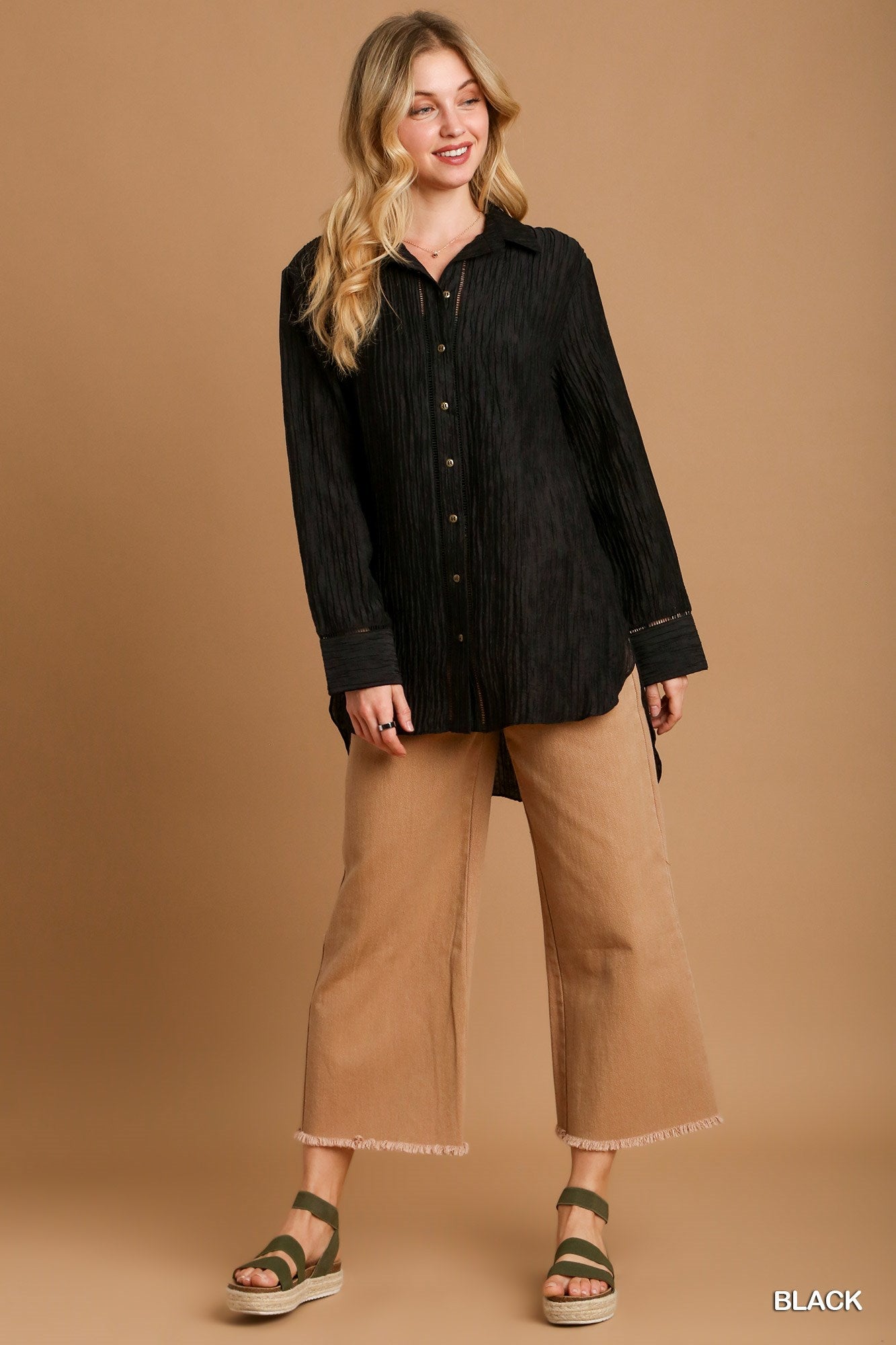 Woman wearing a black shirt and tan pants against a brown background