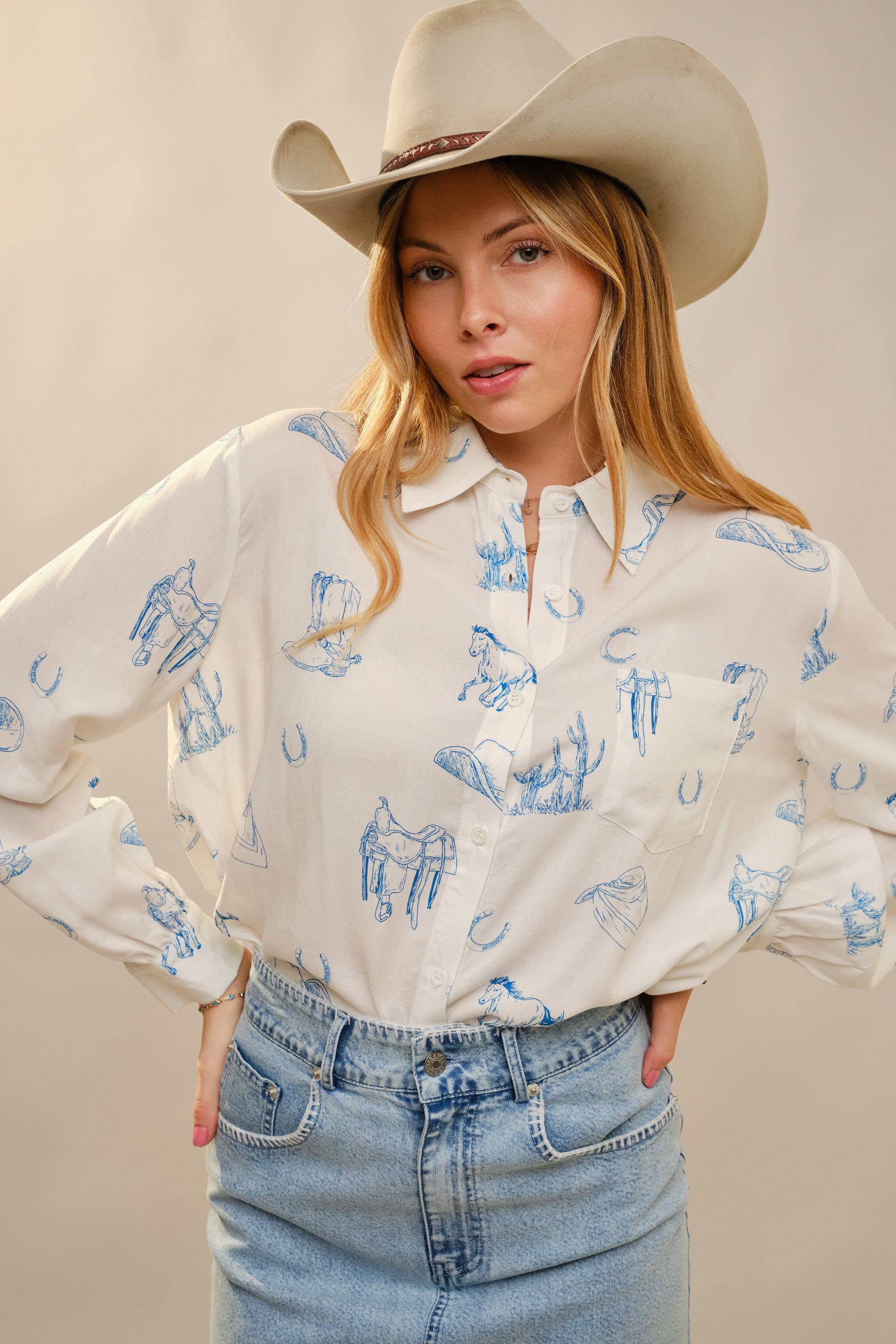 Woman wearing a white blouse with blue patterns and a cowboy hat against a plain background