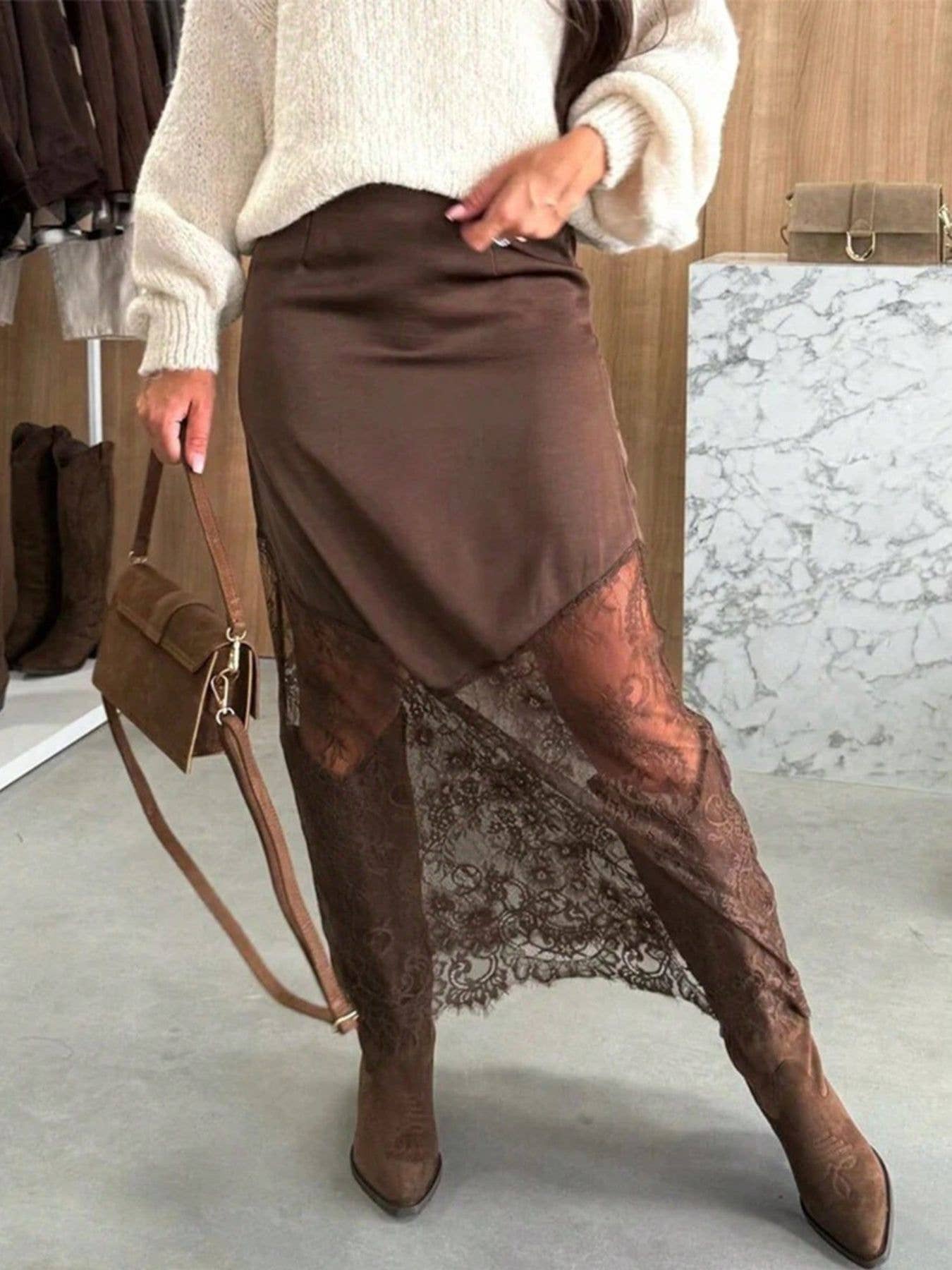 Person wearing a brown skirt with lace detailing and brown boots, holding a brown handbag.
