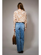 Person wearing a patterned blouse and blue jeans, standing against a plain background