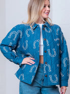 Front view of denim-blue quilted jacket with white horseshoe print and button front on model.