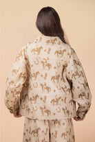Person wearing a beige shirt with horse pattern on a beige background
