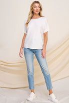 Woman wearing a white top and light blue jeans against a beige draped fabric background