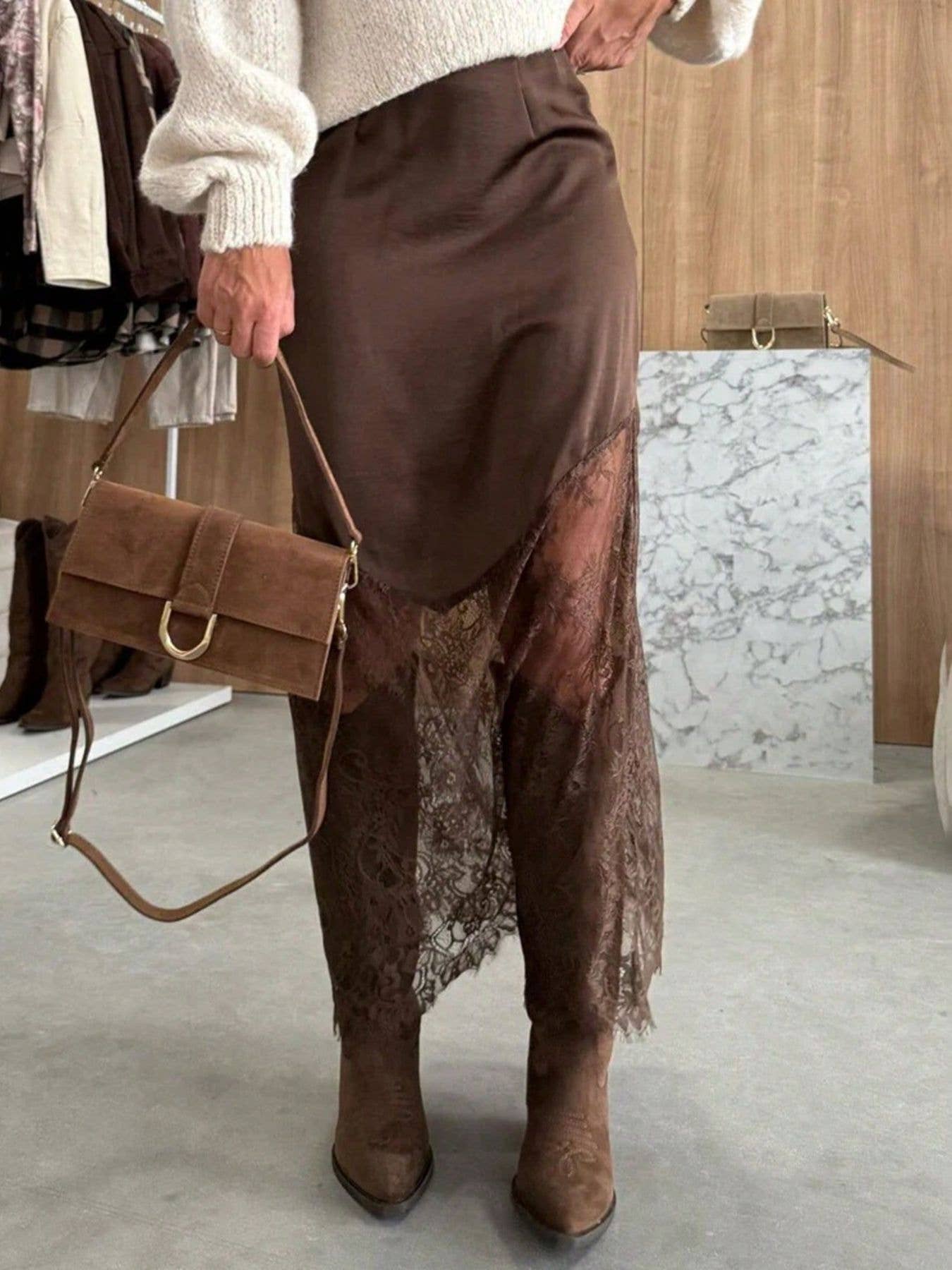 Person wearing brown skirt and boots holding a brown handbag indoors.