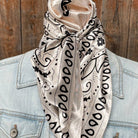 Beige scarf with black patterns draped over a light blue denim jacket against a wooden background