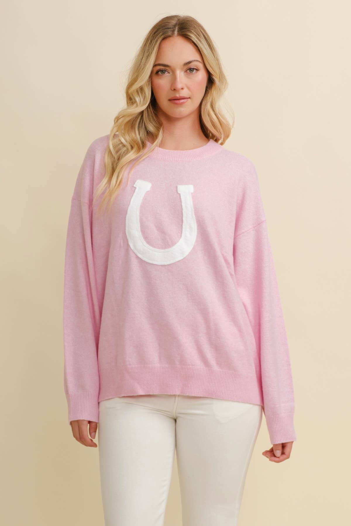 Woman wearing a pink long-sleeve shirt with a white horseshoe logo on a beige background