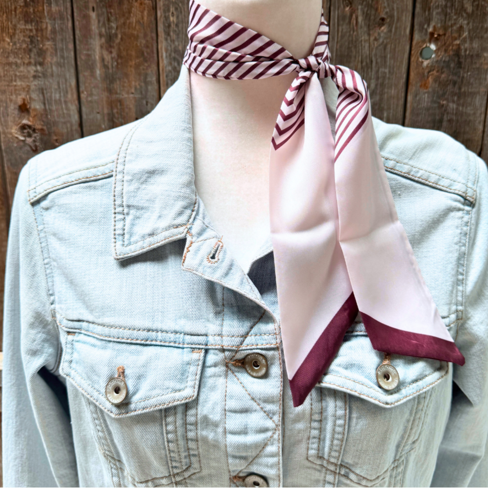 Person wearing a light blue denim jacket with burgundy and cream striped scarf around their neck against a wooden background.