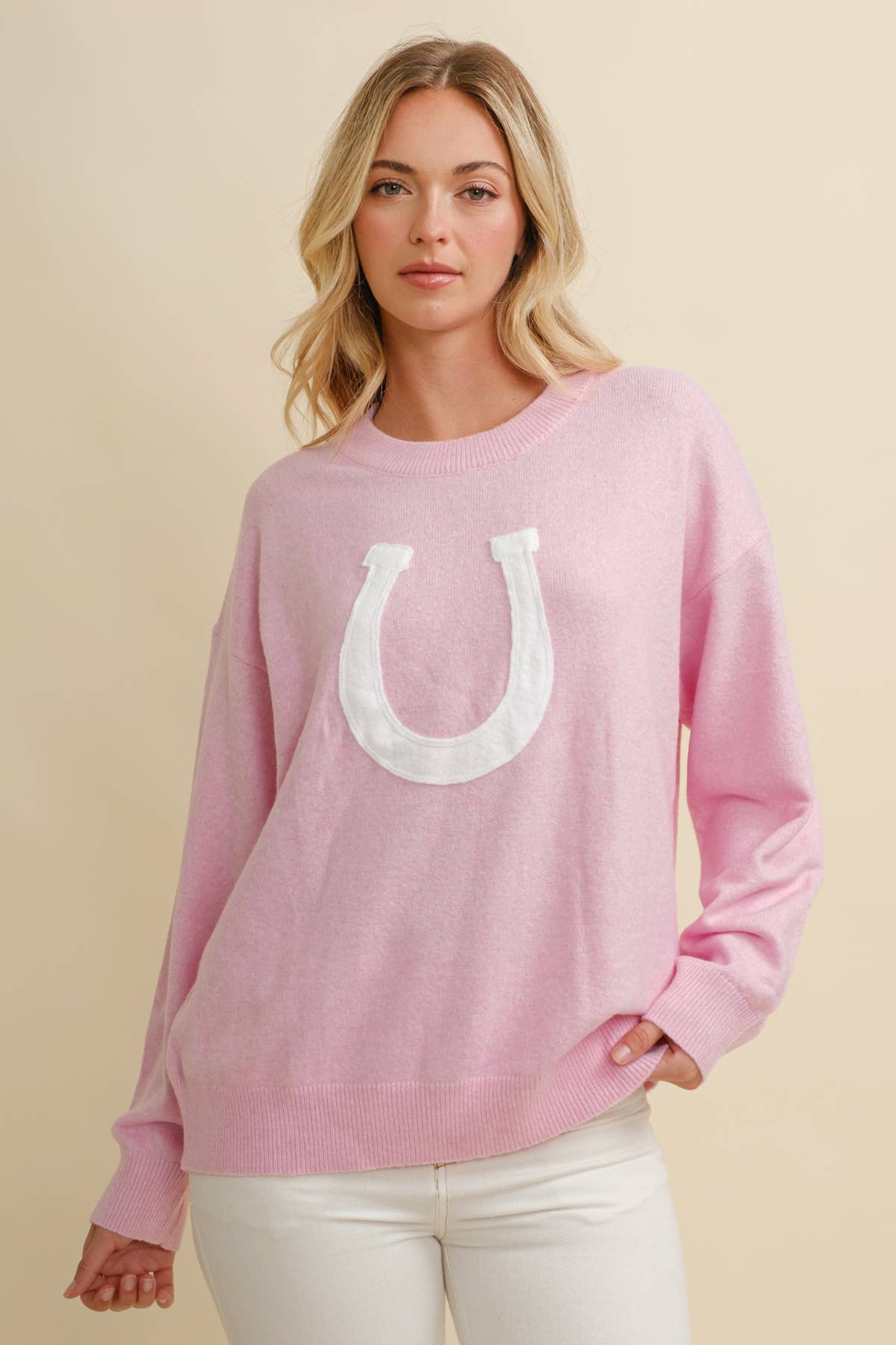 Woman wearing a pink sweatshirt with a white horseshoe design on a beige background