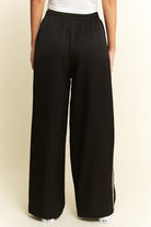 Black wide-leg pants with a side stripe on a beige background
